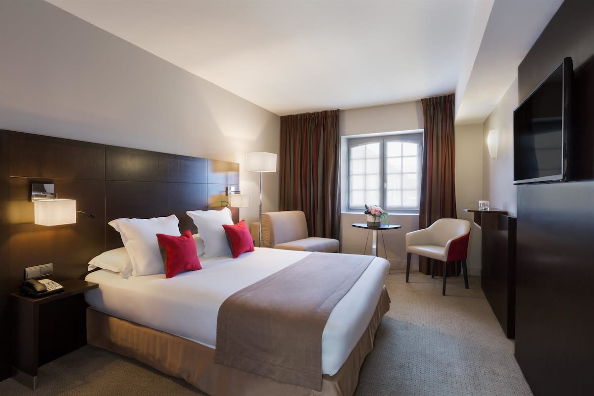Quarto de hotel com uma cama grande, luminárias de cabeceira, televisão, escrivaninha e uma cadeira.