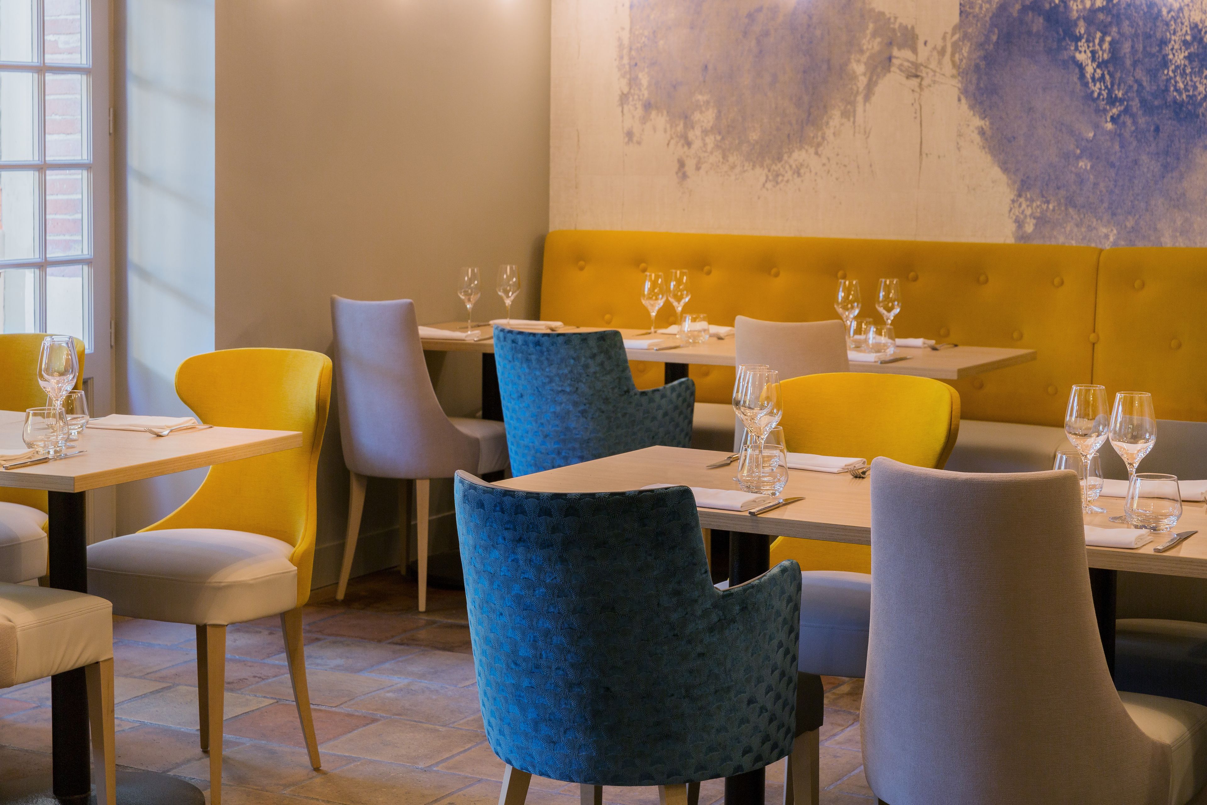 A restaurant interior with yellow and blue chairs, white tables, and a yellow cushioned bench.