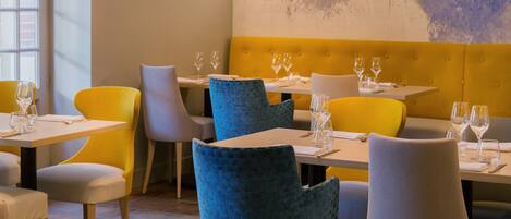 A restaurant interior with yellow and blue chairs, white tables, and a yellow cushioned bench.