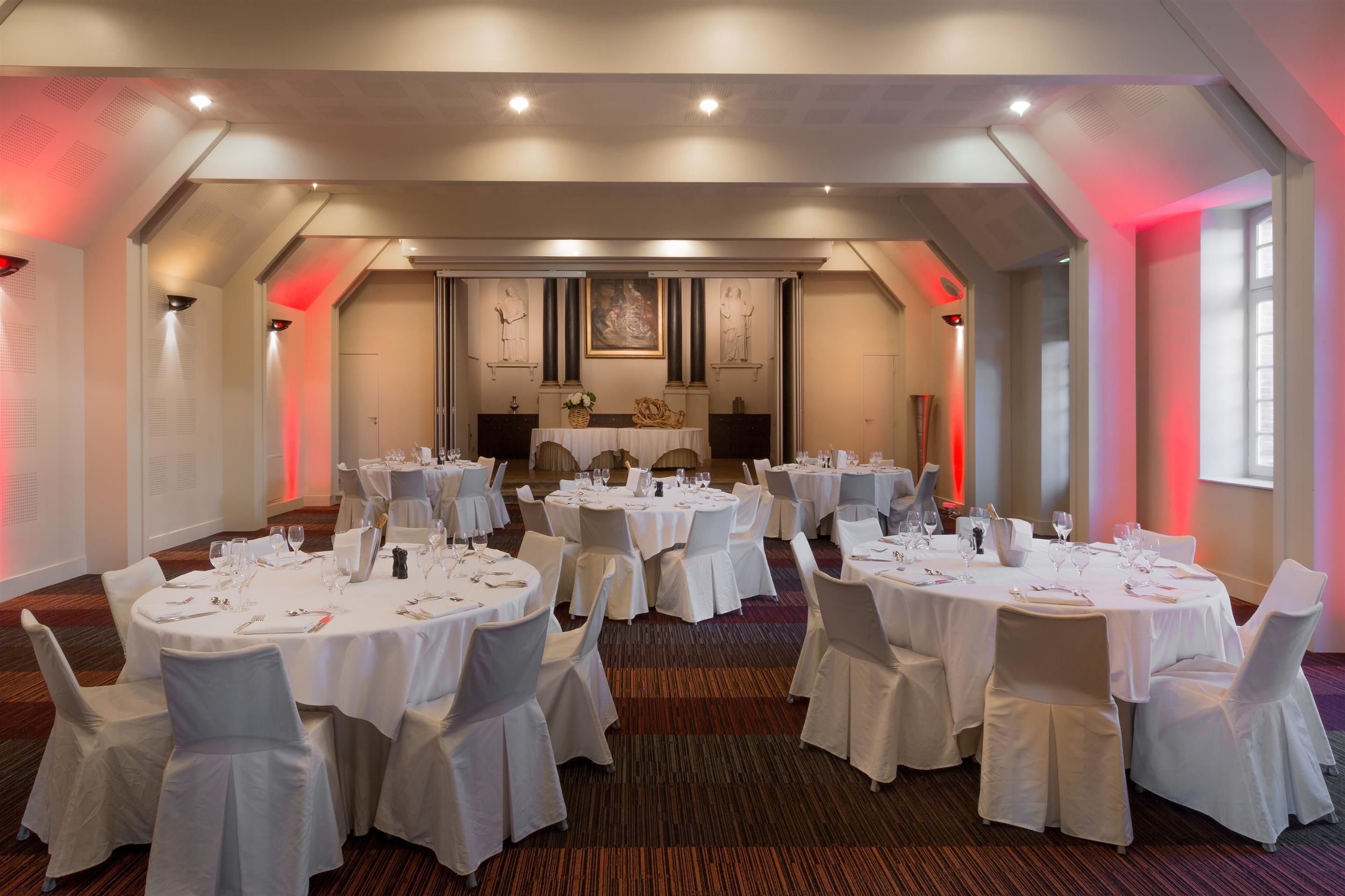 A banquet hall with round tables set for dining, white chairs, and a central stage area.