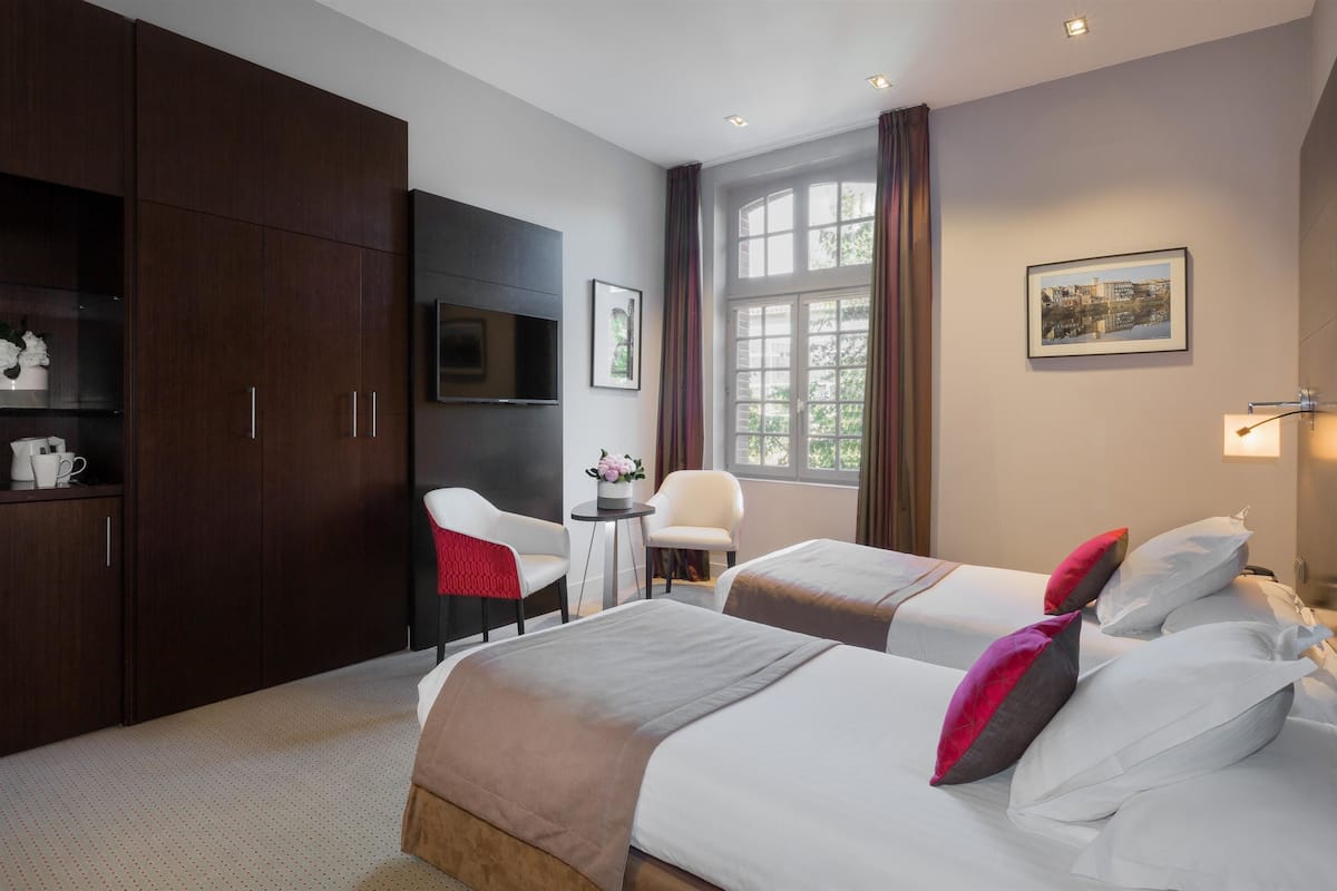 Quarto de hotel com duas camas, uma escrivaninha, uma cadeira, uma televisão e uma janela com cortinas.