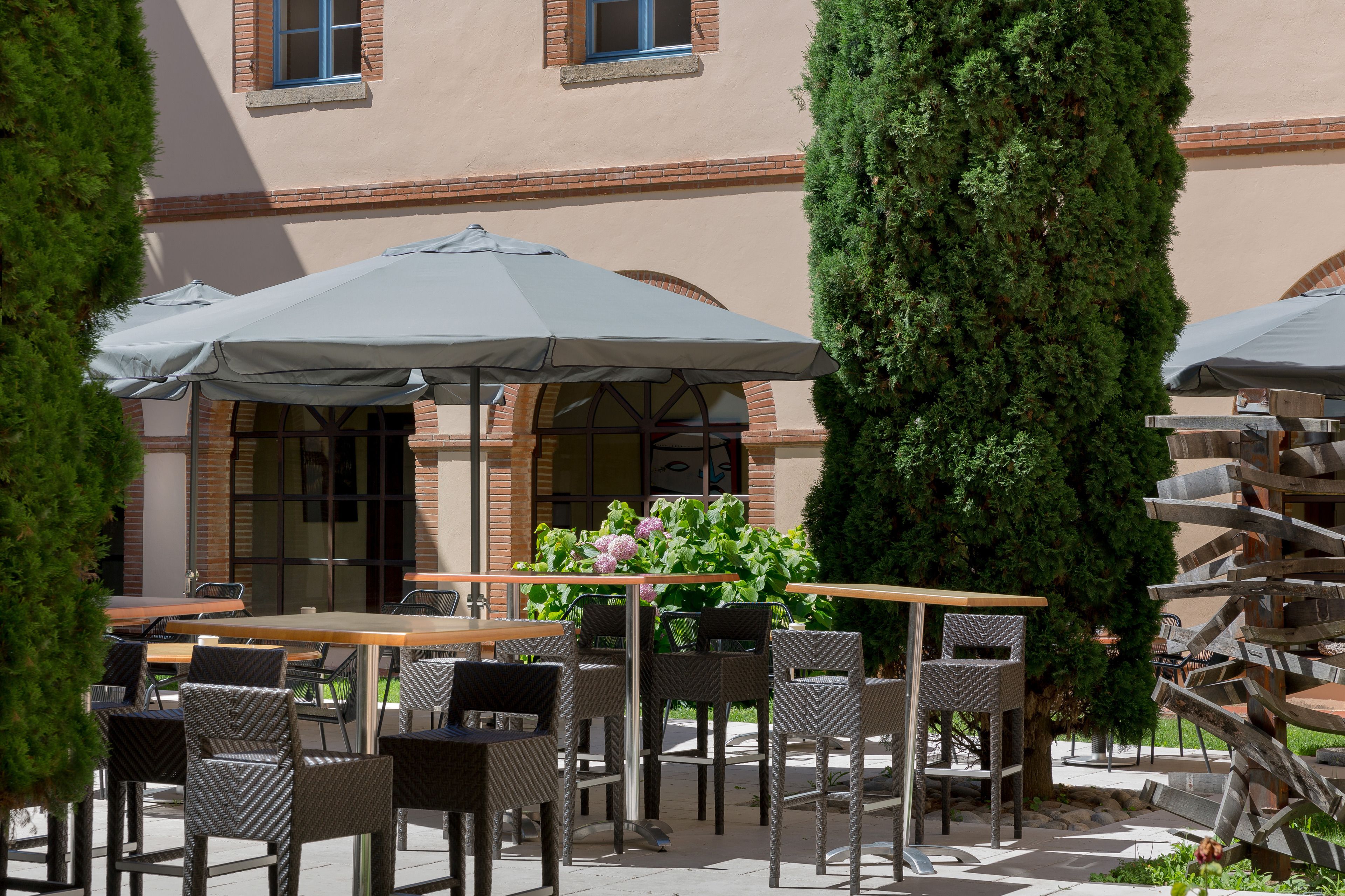 An outdoor patio with wicker furniture, umbrellas, and a brick building in the background.