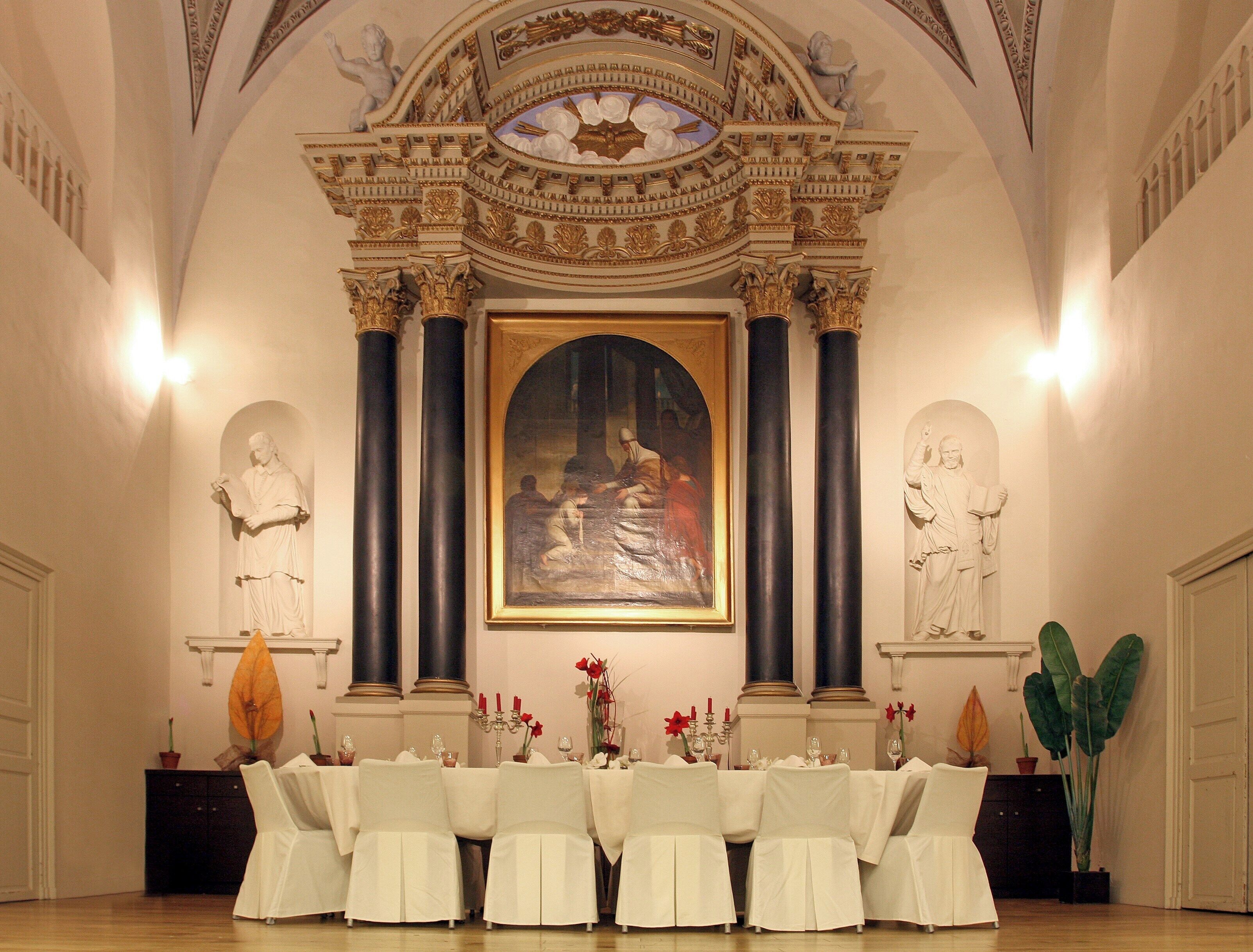 An ornate dining room with a large painting, classical statues, and a formal table setting.