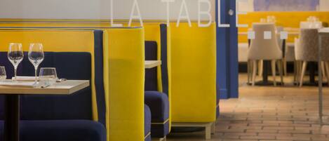 A restaurant interior with yellow and blue booths, tables with glasses and cutlery, and a tiled floor.