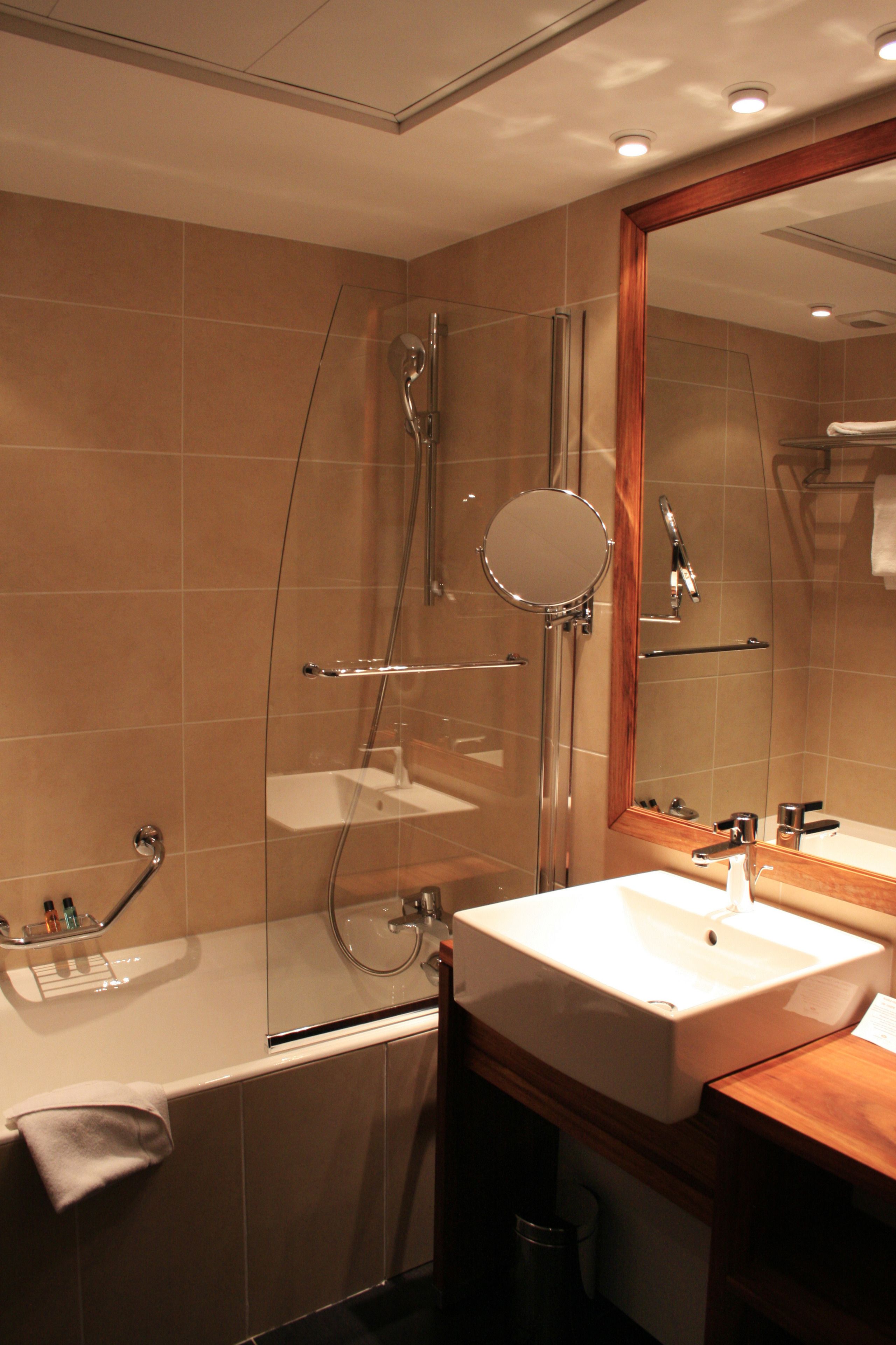 Een moderne badkamer met een douche met glazen wanden, een witte wastafel en een houten opbergmeubel.
