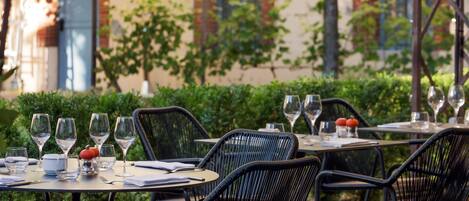 Mesas de comedor al aire libre con sillas, copas de vino y un menú.