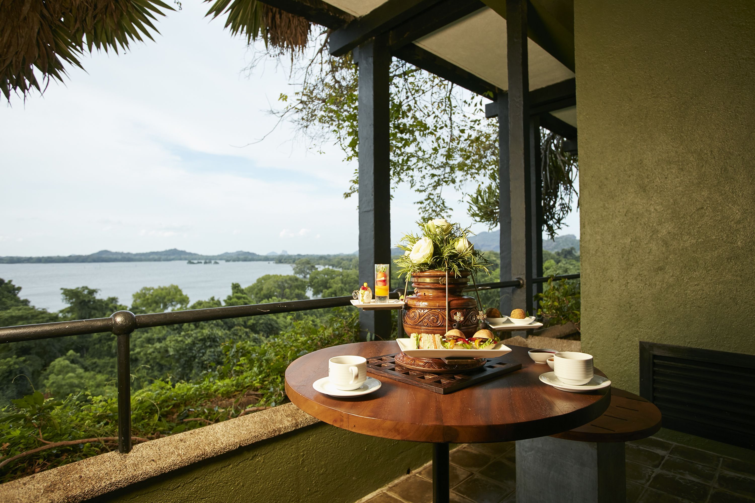 Uma mesa de madeira redonda com uma chávena branca, um prato com sanduíches e um vaso decorativo com flores.