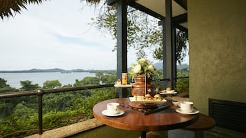 Uma mesa de madeira redonda com uma chávena branca, um prato com sanduíches e um vaso decorativo com flores.