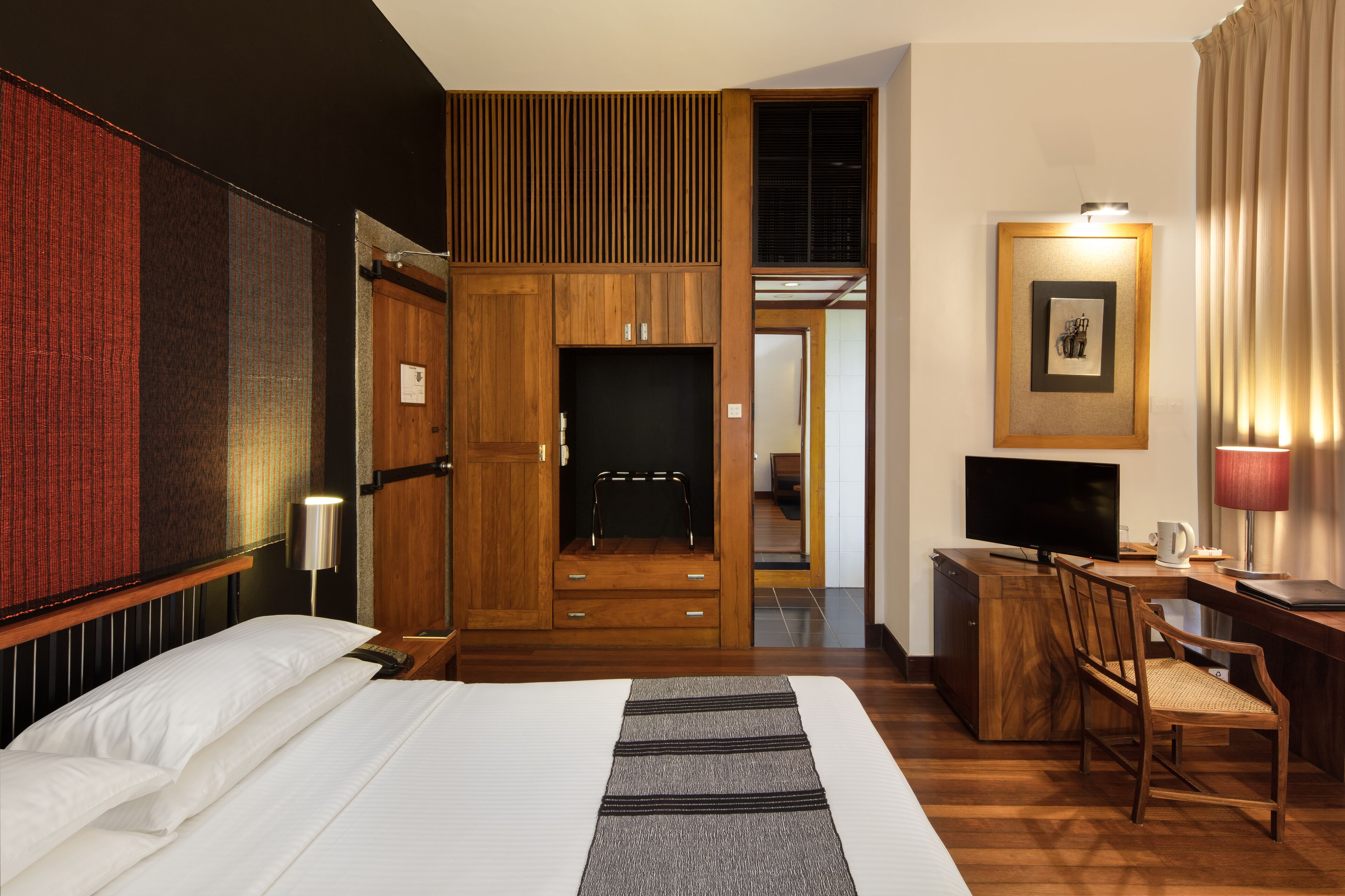 A hotel room with a bed, a desk with a television, a chair, and a wardrobe.