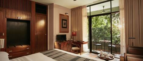 Habitación de hotel con una cama grande, un escritorio con computadora, un televisor y un balcón con mesa y sillas.