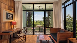 A room with a wooden desk, chair, and sofa, a small table, and a view through large windows. - Heritance Kandalama (Kandalama)