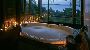 A large, oval-shaped hot tub with a view of a body of water and trees through a large window. - Heritance Kandalama (Kandalama)