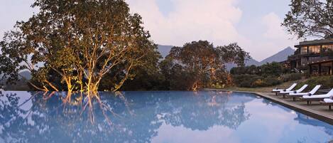 A serene pool area with lounge chairs, trees, and a building with illuminated windows.