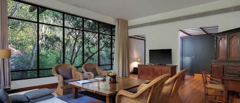 A spacious room with large windows, wicker furniture, a wooden dining table, and a television.