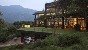 A modern multi-story building with large windows, a rooftop terrace, and a dining area with outdoor seating. - Heritance Kandalama (Kandalama)