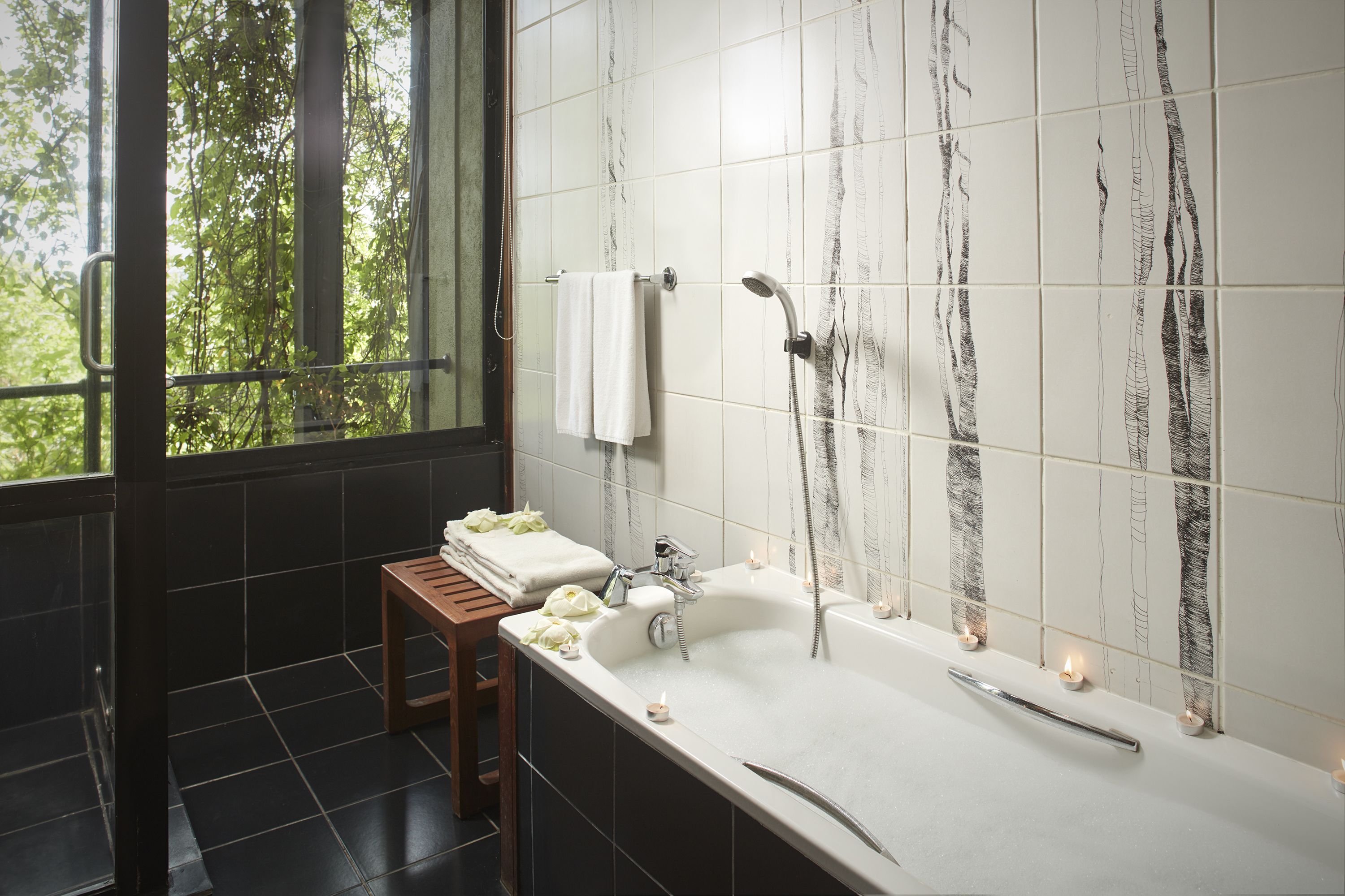 A bathroom with a large bathtub, a wooden stool, and a window with a view of trees.