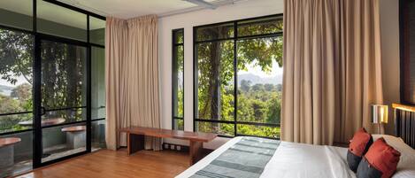 Camera da letto con un letto grande, una ventola a soffitto, una panca e vista sul verde attraverso ampie finestre.