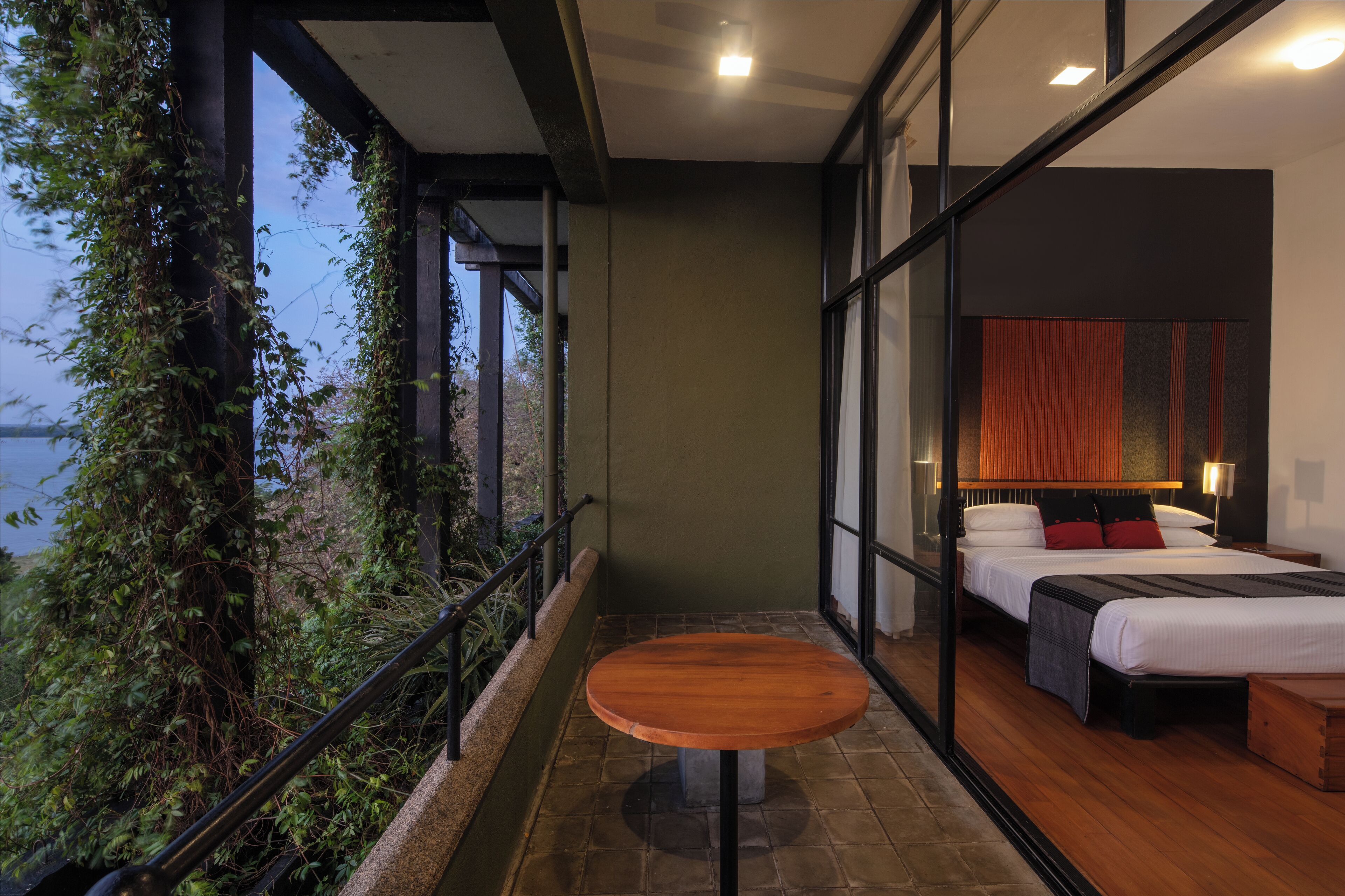 A balcony with a wooden table and a bed with a red and black headboard.
