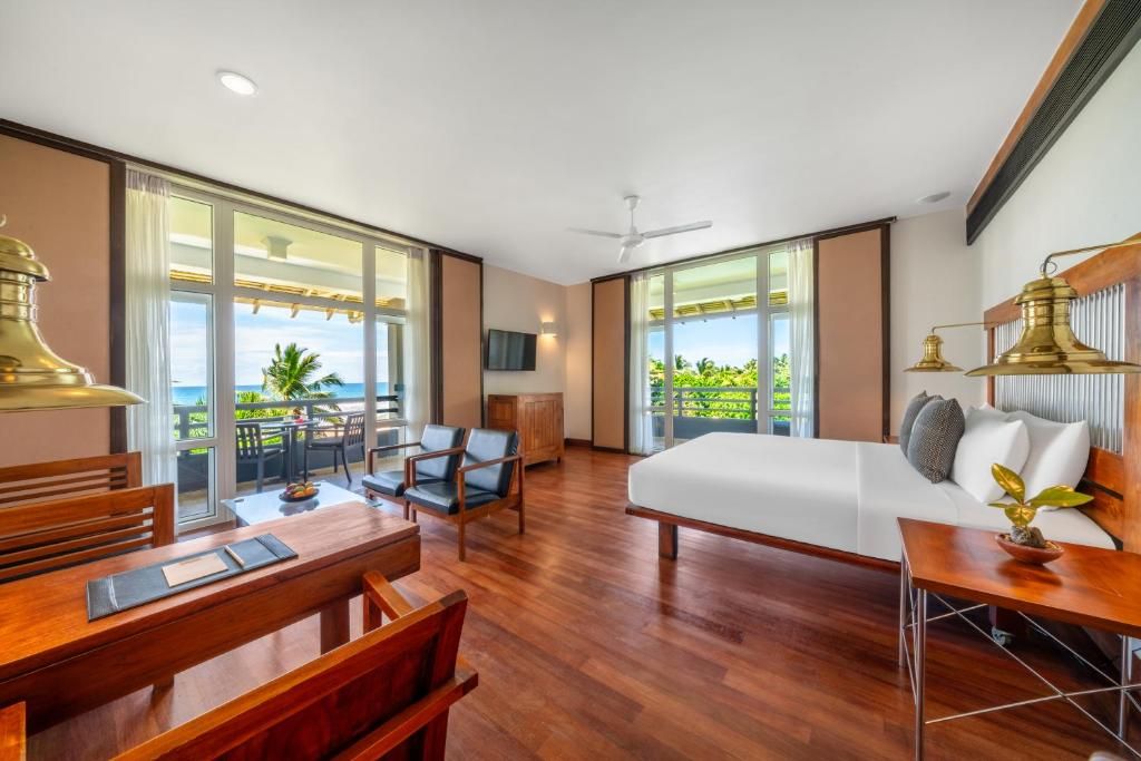 A hotel room with a large bed, a desk, a chair, a sofa, and a balcony with a view.