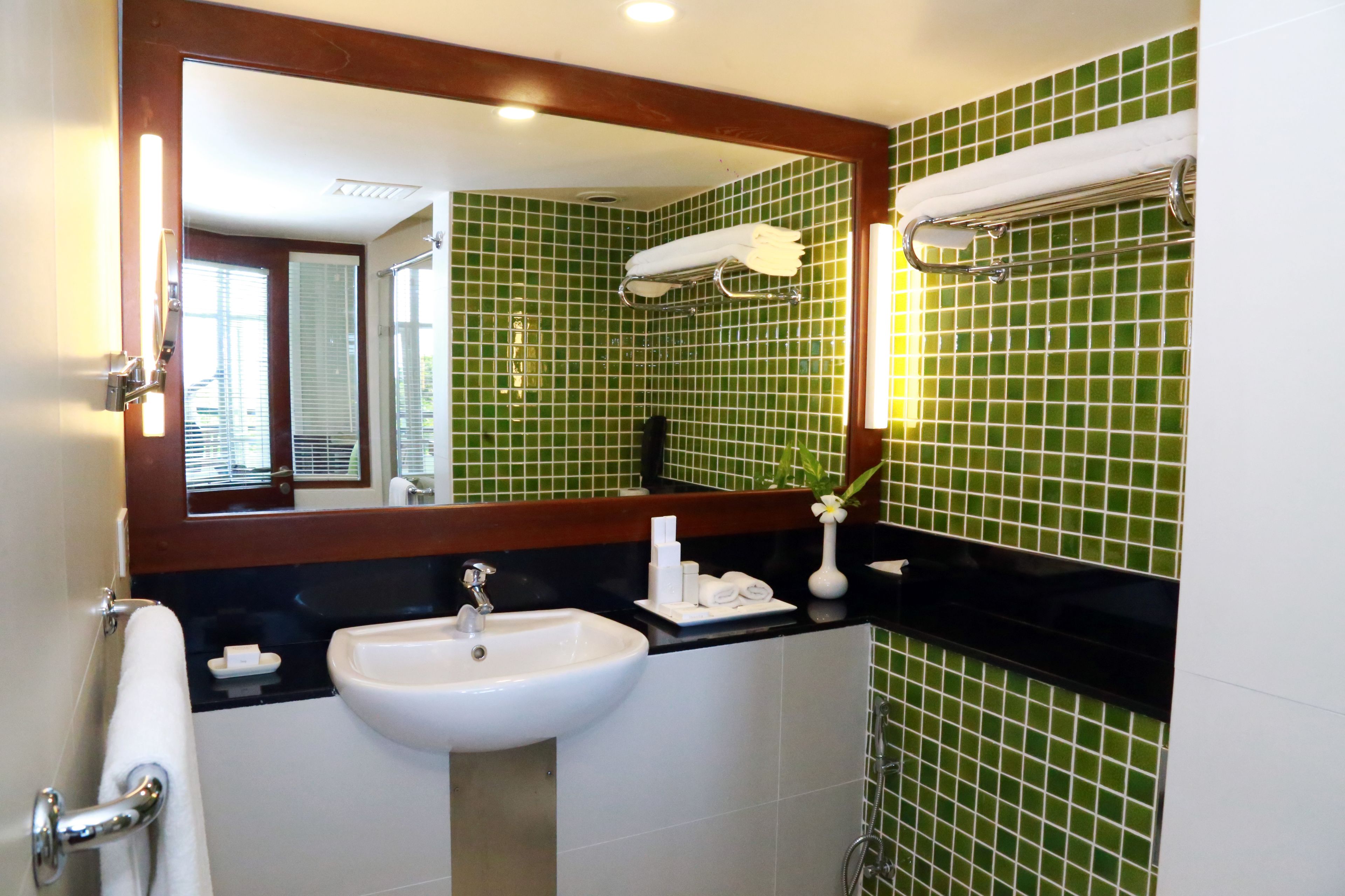 A bathroom with a white sink, green tiled walls, a large mirror, and a towel rack.
