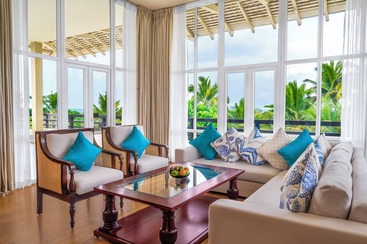 A spacious room with a large window, a wooden coffee table, a sofa, and two chairs.