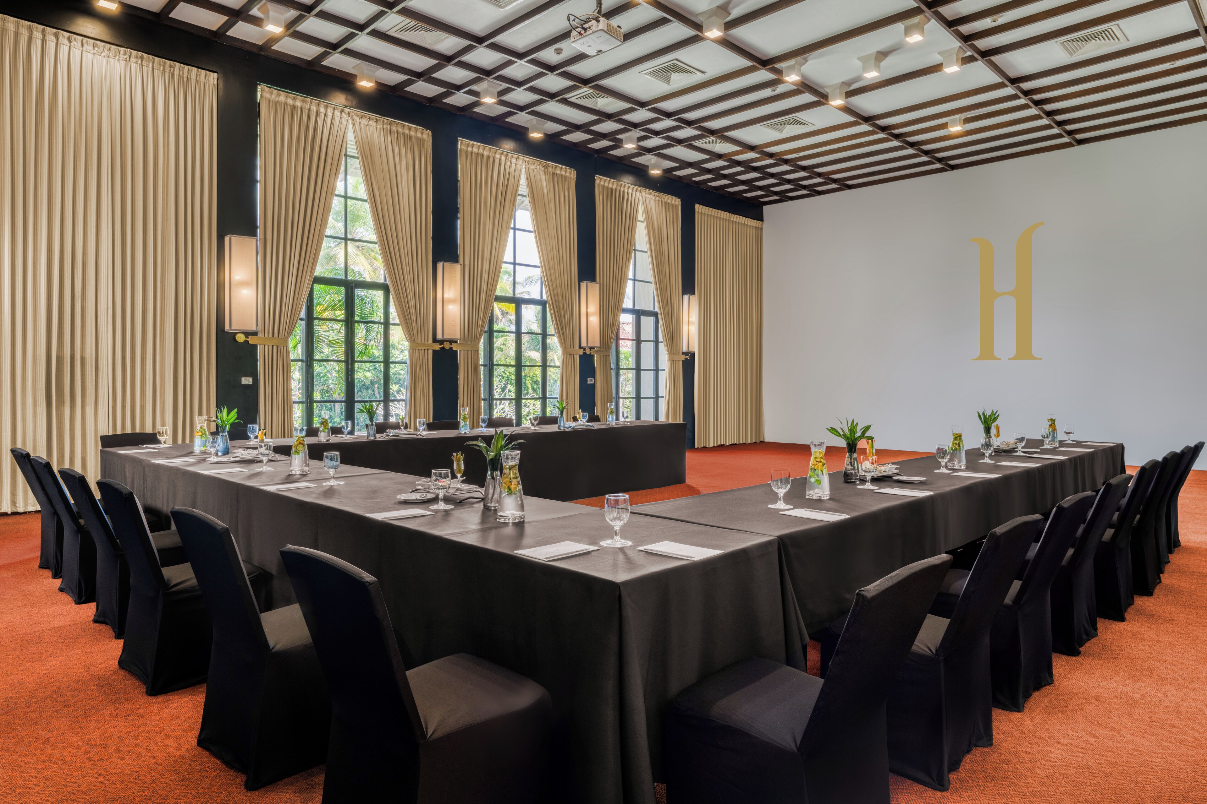 Un salón de conferencias con una larga mesa, sillas negras y ventanas amplias con cortinas.