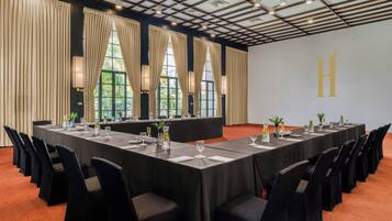 Una sala conferenze con un lungo tavolo, sedie nere e ampie finestre con tende.