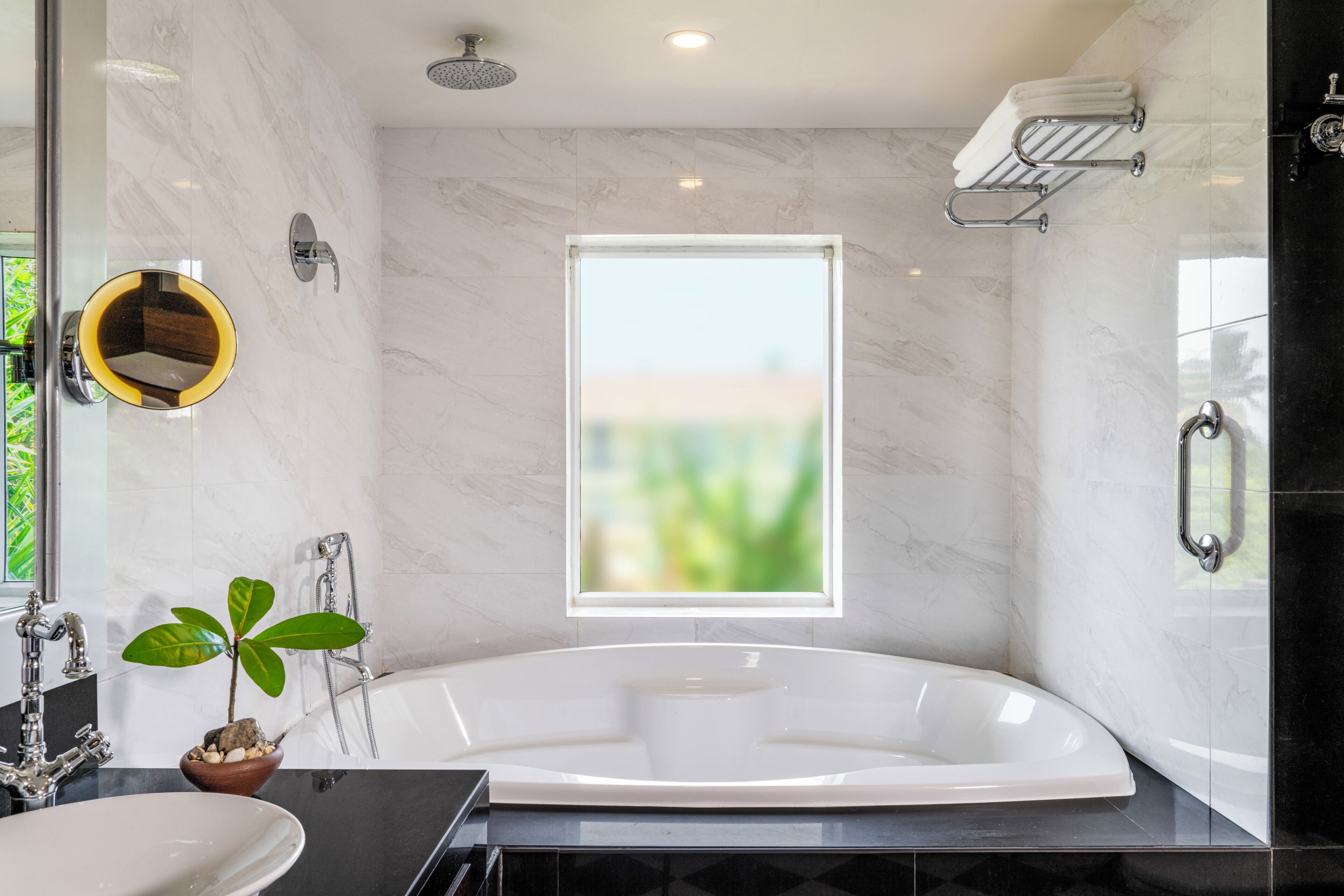 Un baño moderno con una bañera grande, un lavabo, un espejo y una ventana con vistas a zonas verdes.