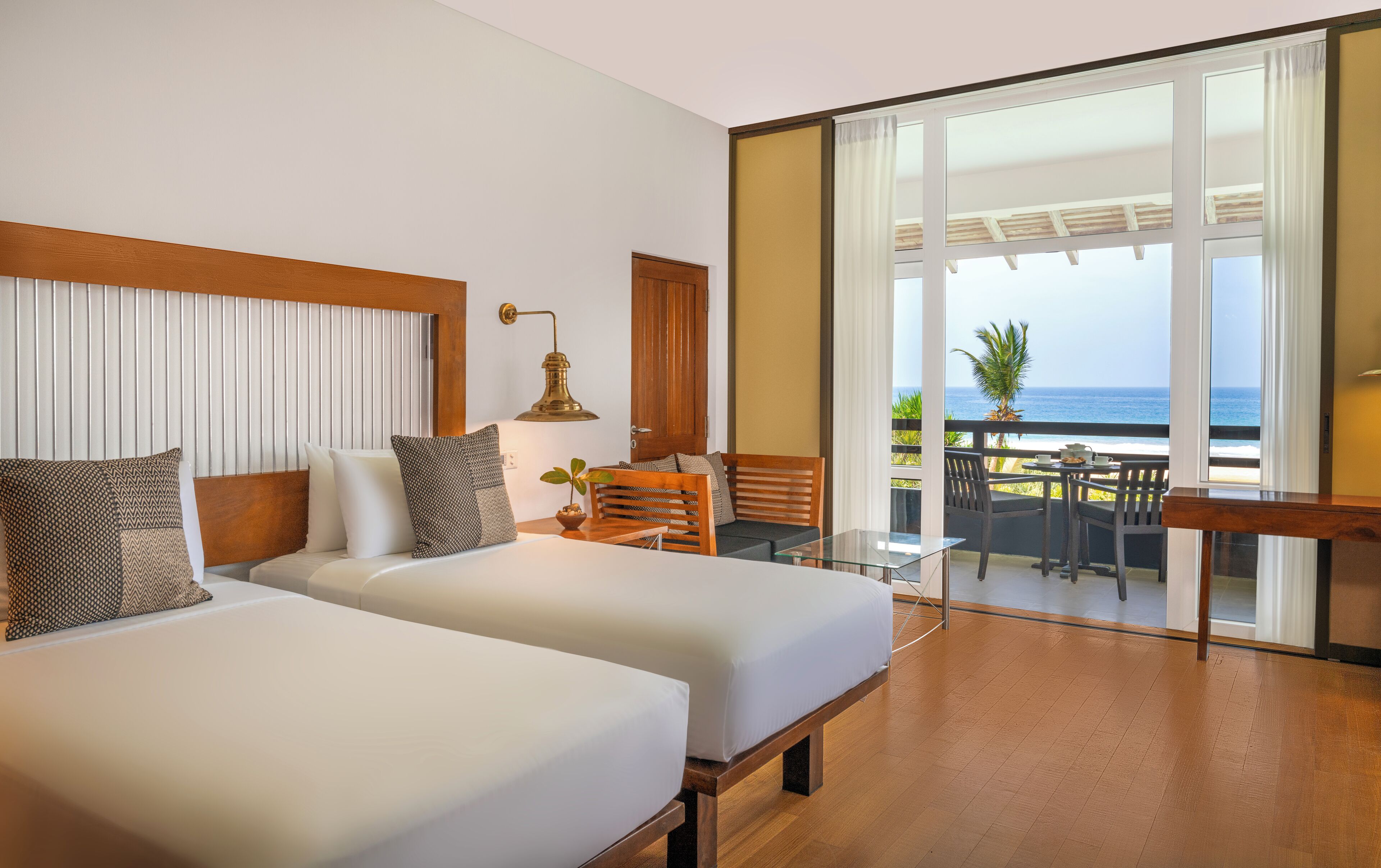 Une chambre d’hôtel avec deux lits, un balcon avec une table et des chaises, et une vue sur l’océan.