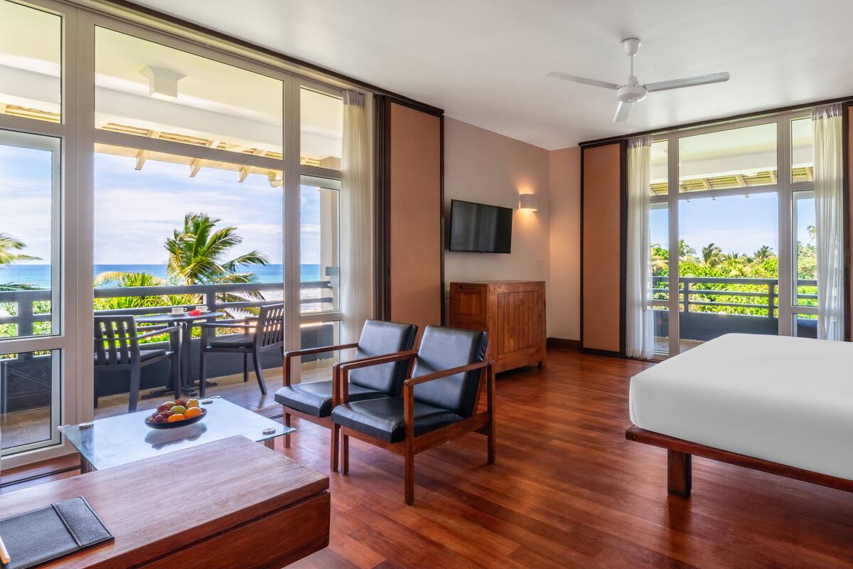 A hotel room with a large balcony, wooden furniture, a flat-screen TV, and a bed.