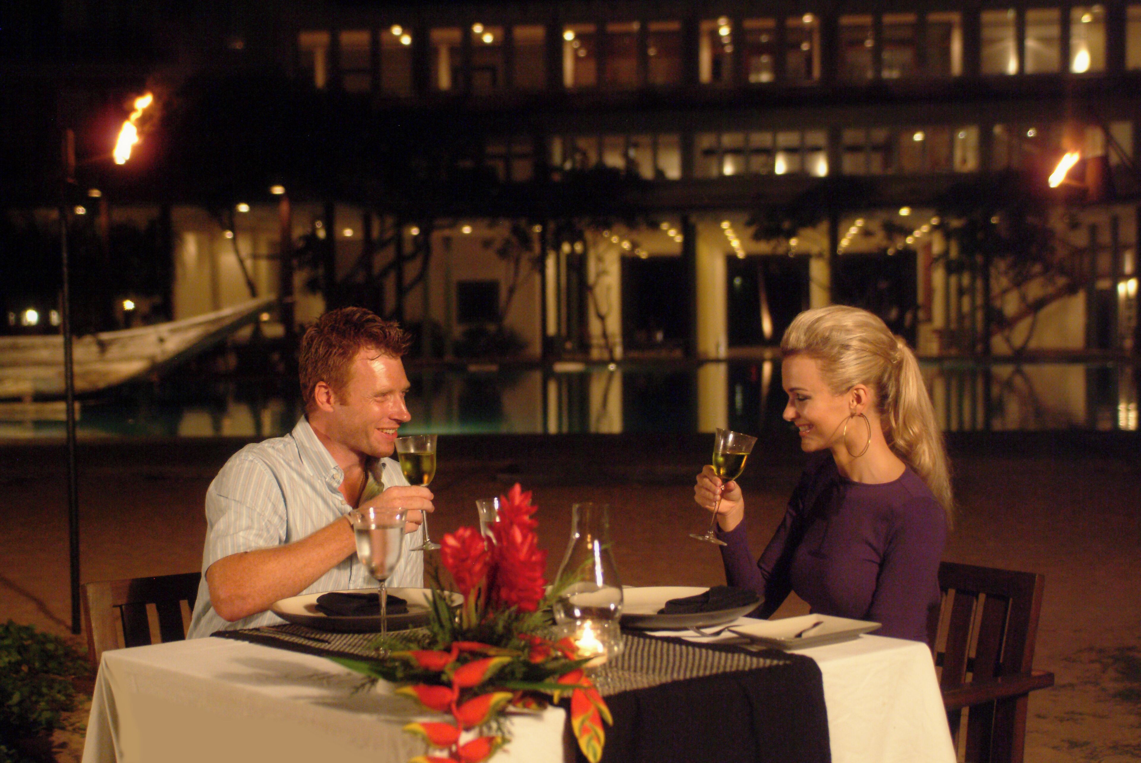A couple dining at an outdoor table with a view of a building and a staircase.