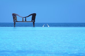 A bench by a pool with a clear view of the ocean.