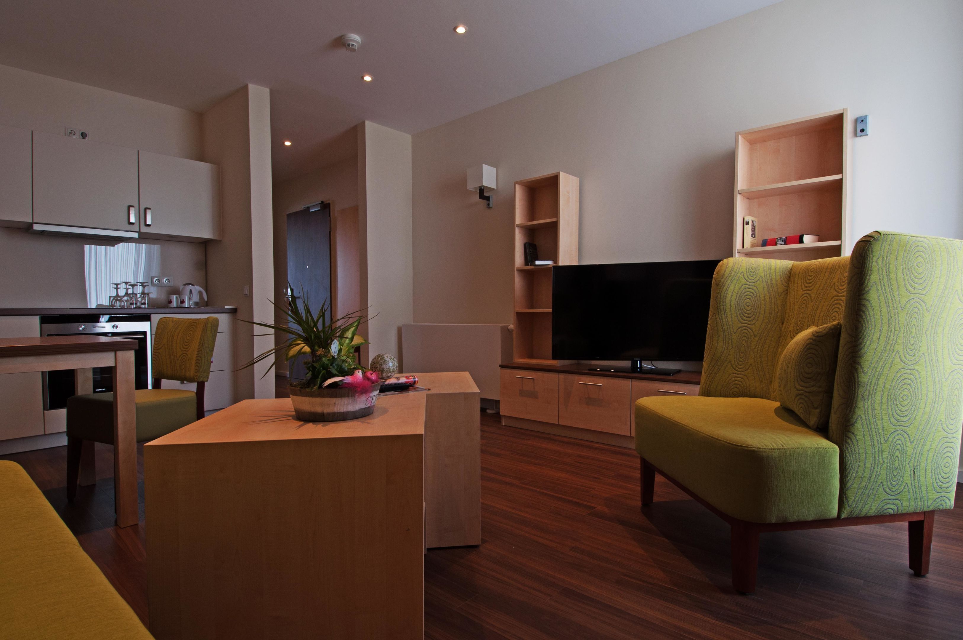 A modern living room with a flat-screen TV, a dining area with a table and chairs, and a kitchen with cabinets and appliances.