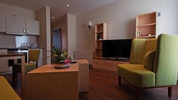 A modern living room with a flat-screen TV, a dining area with a table and chairs, and a kitchen with cabinets and appliances.