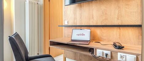 Una habitación de hotel moderna con un escritorio de madera, una computadora portátil, un televisor de pantalla plana y una silla.