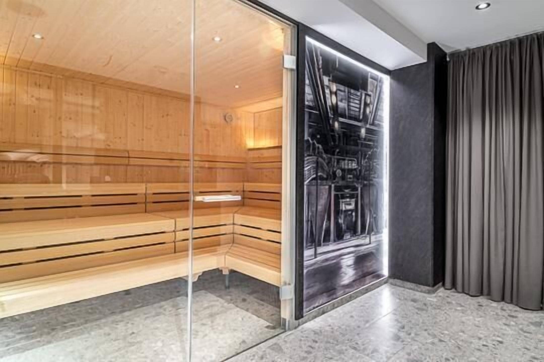 A sauna room with wooden benches, a glass wall, and a dark curtain.