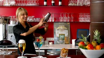 Ein Barkeeper bereitet ein Getränk zu, im Hintergrund sind Regale mit Weingläsern und Flaschen zu sehen.