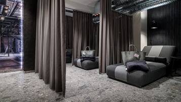 A modern hotel room with a sofa, a chair, a small table, and a view of the outside.