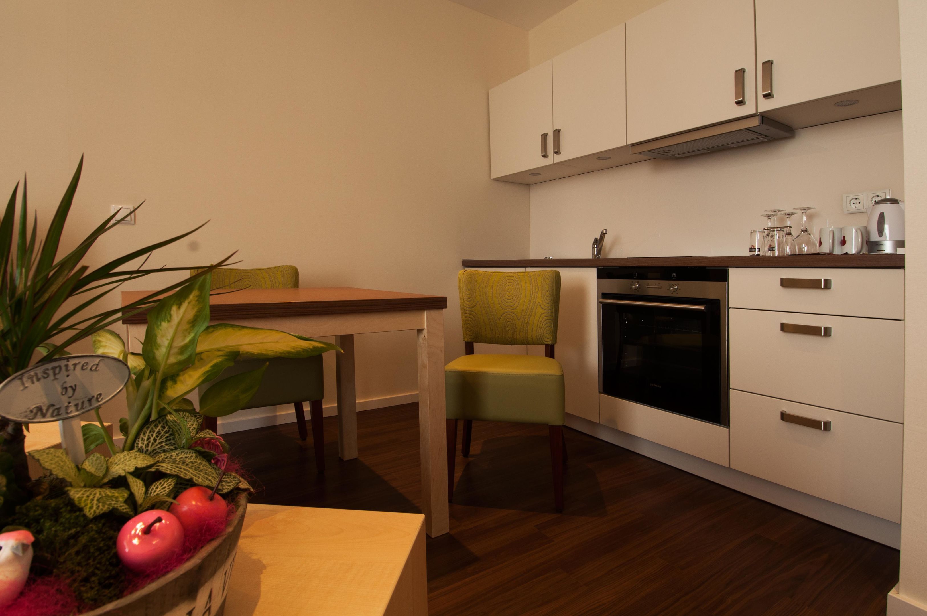 A modern kitchen with white cabinets, a built-in oven, and a dining area with a table and chairs.