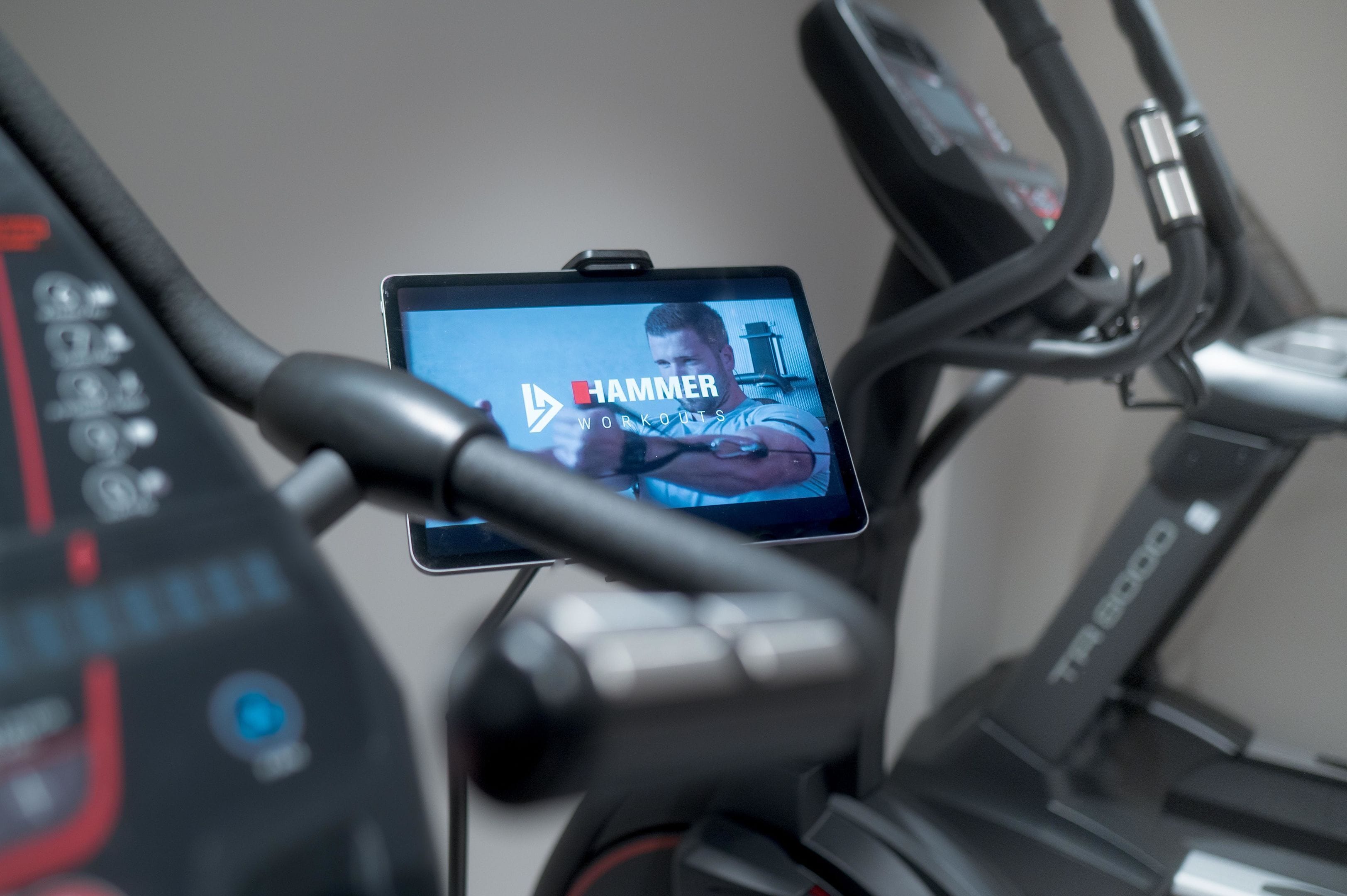 Ein Laufband mit einem digitalen Bildschirm, der 'HAMMER WORKOUTS' anzeigt, und ein Smartphone, das am Lenker befestigt ist.