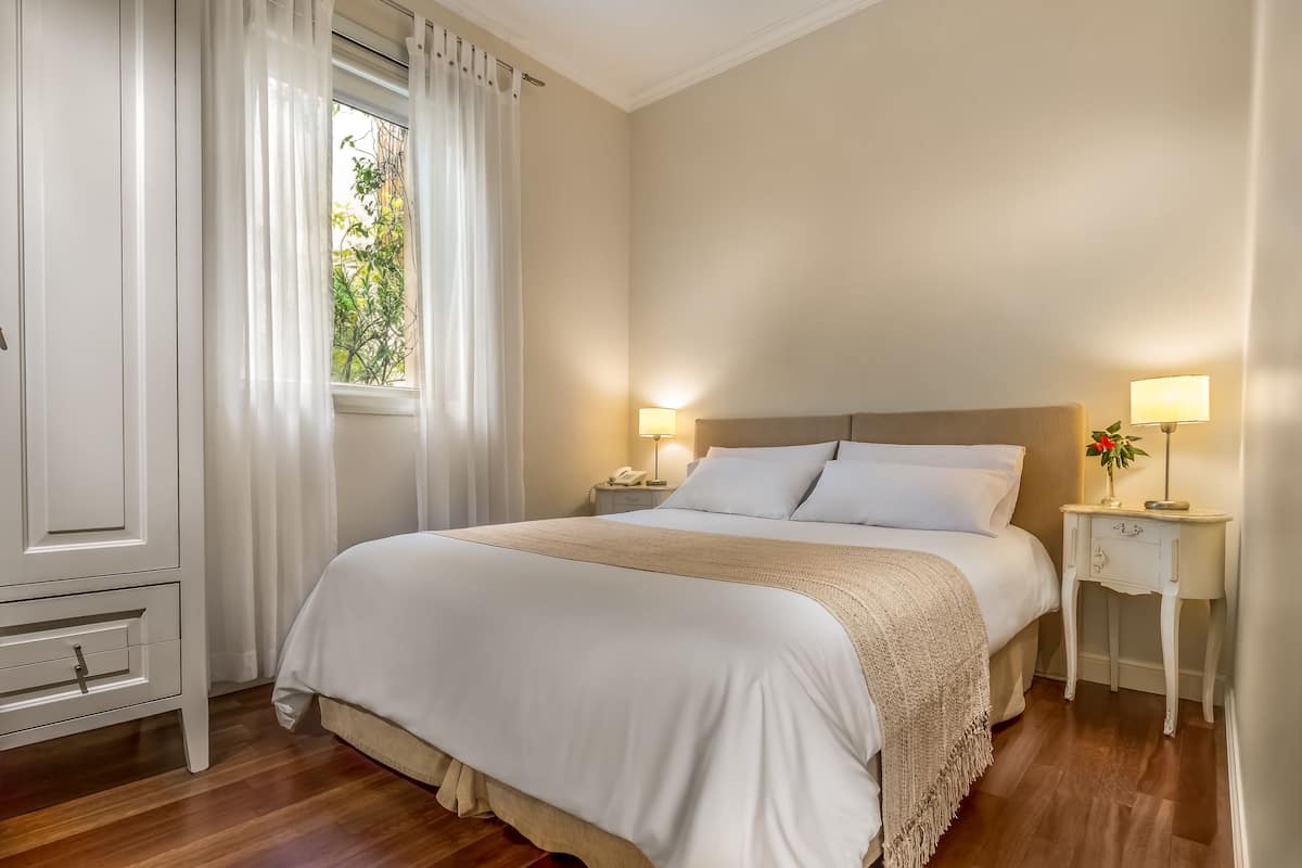 A neatly arranged bedroom with a bed, bedside tables, and a window with curtains.