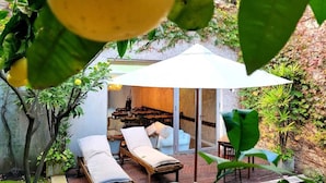 A private outdoor lounge with a wooden deck, two lounge chairs, a table, and a large umbrella providing shade. - 248 Finisterra Hotel Boutique Argentino (Buenos Aires)