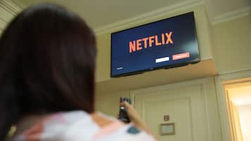 A person using a remote control in front of a television displaying the Netflix logo.
