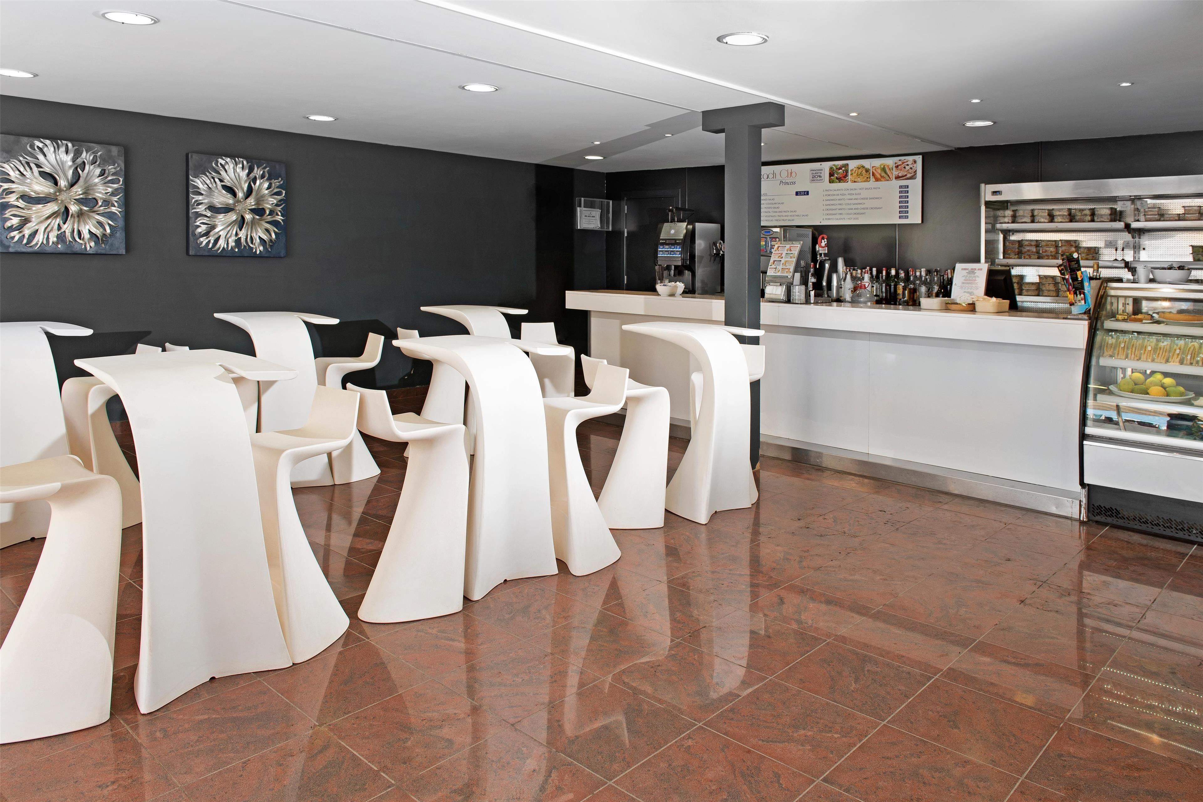 Un interior de cafetería moderno con sillas blancas, una máquina de café y un panel con la carta.