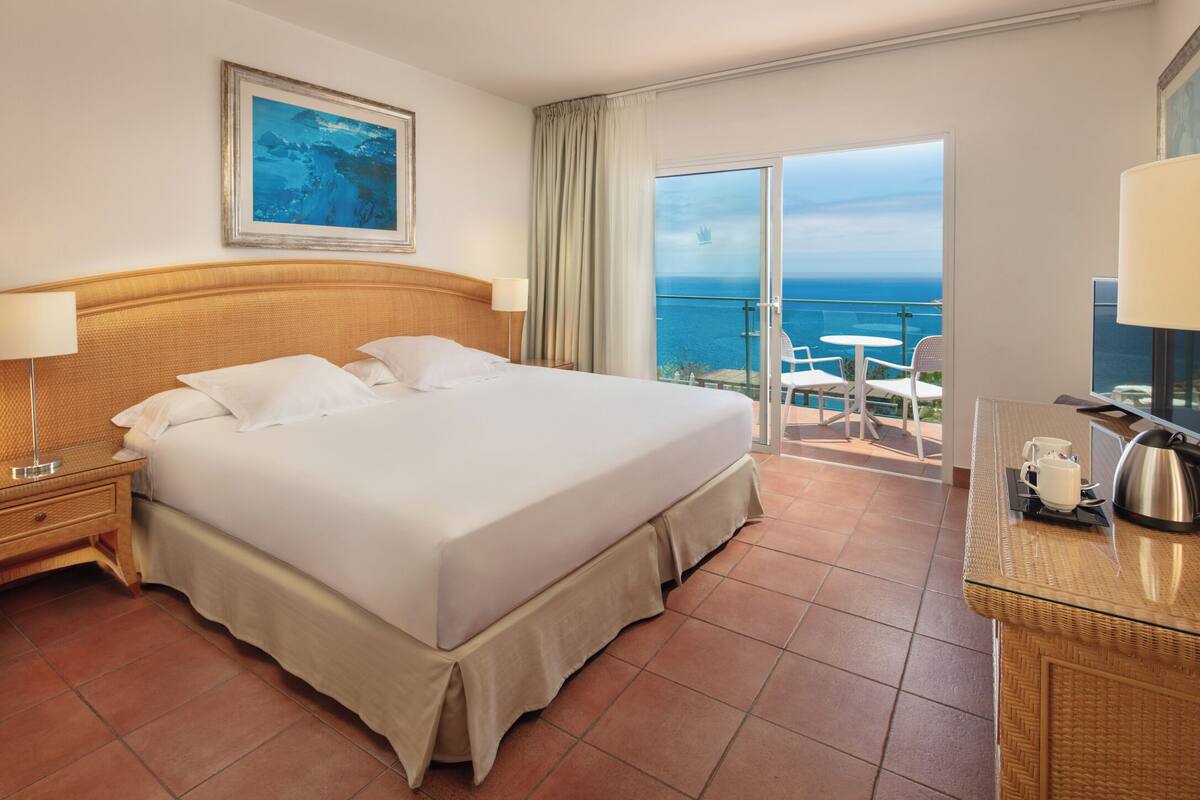 Een hotelkamer met een groot bed, een nachtkastje, een lamp, een salontafel en uitzicht op de oceaan.