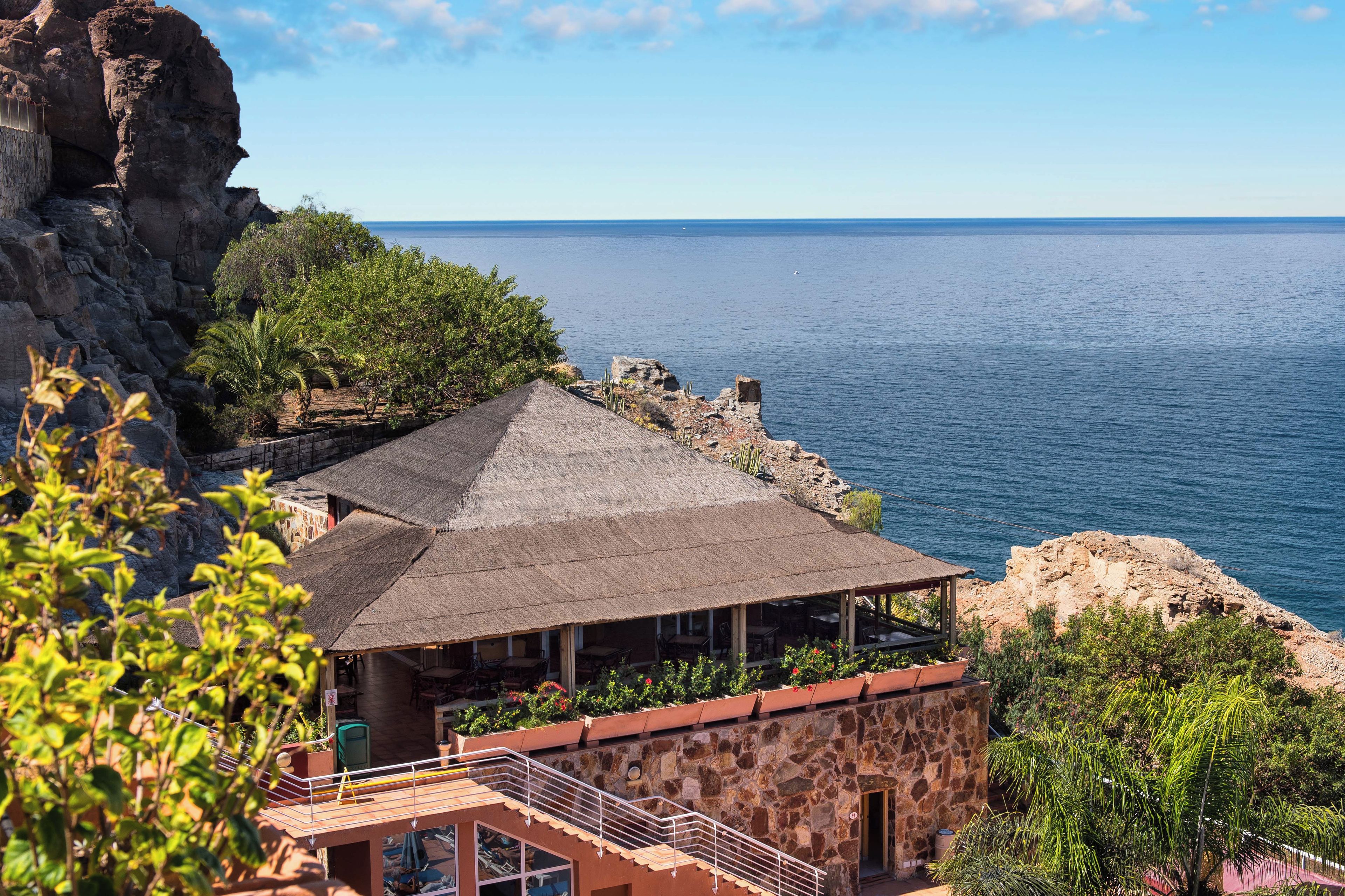 Un edificio costero con fachada de piedra, techo de paja y vista al mar.
