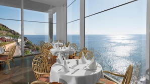 Un espace repas avec des tables rondes, des nappes blanches et des chaises en osier, offrant une vue panoramique sur l’océan.