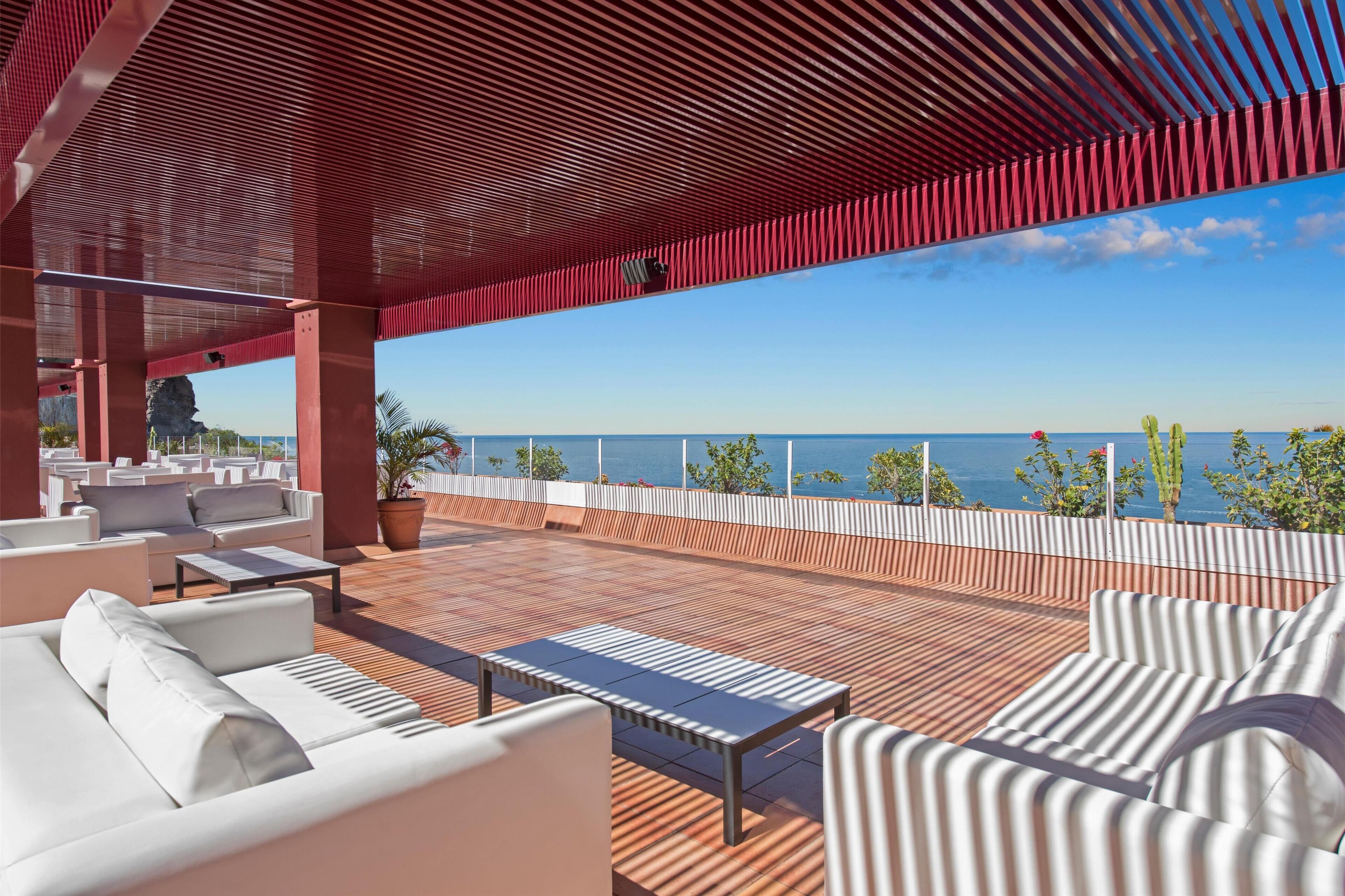 Un espace extérieur moderne, aménagé avec des meubles pour s’asseoir et offrant une vue sur la mer, comprenant des canapés blancs et une terrasse en bois.