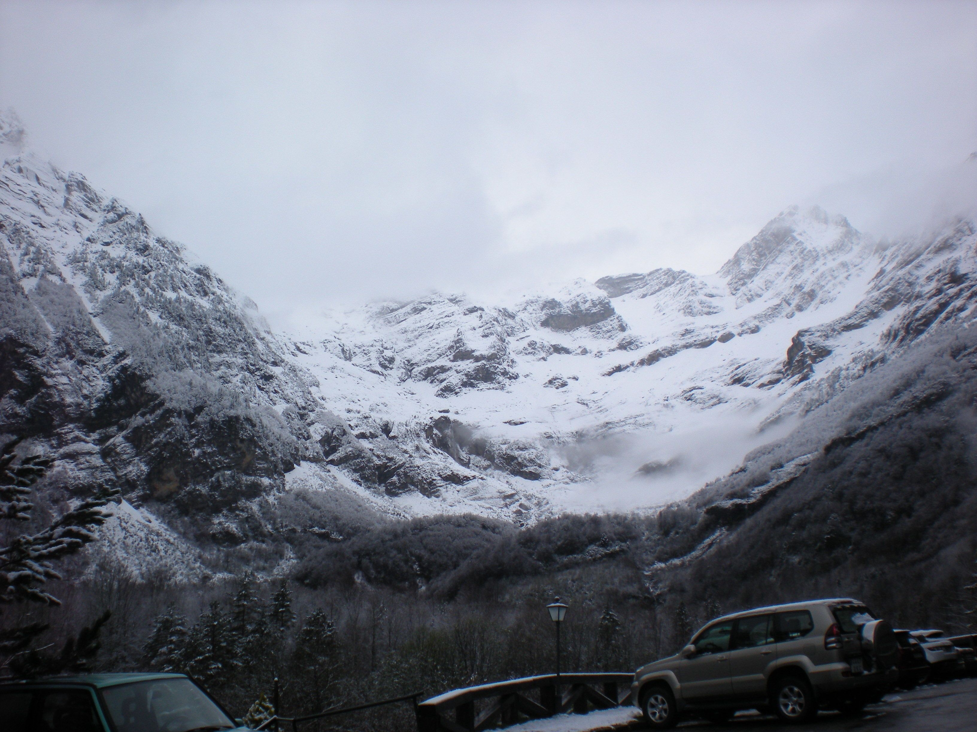 Un paisaje montañoso nevado con un puente y vehículos estacionados.