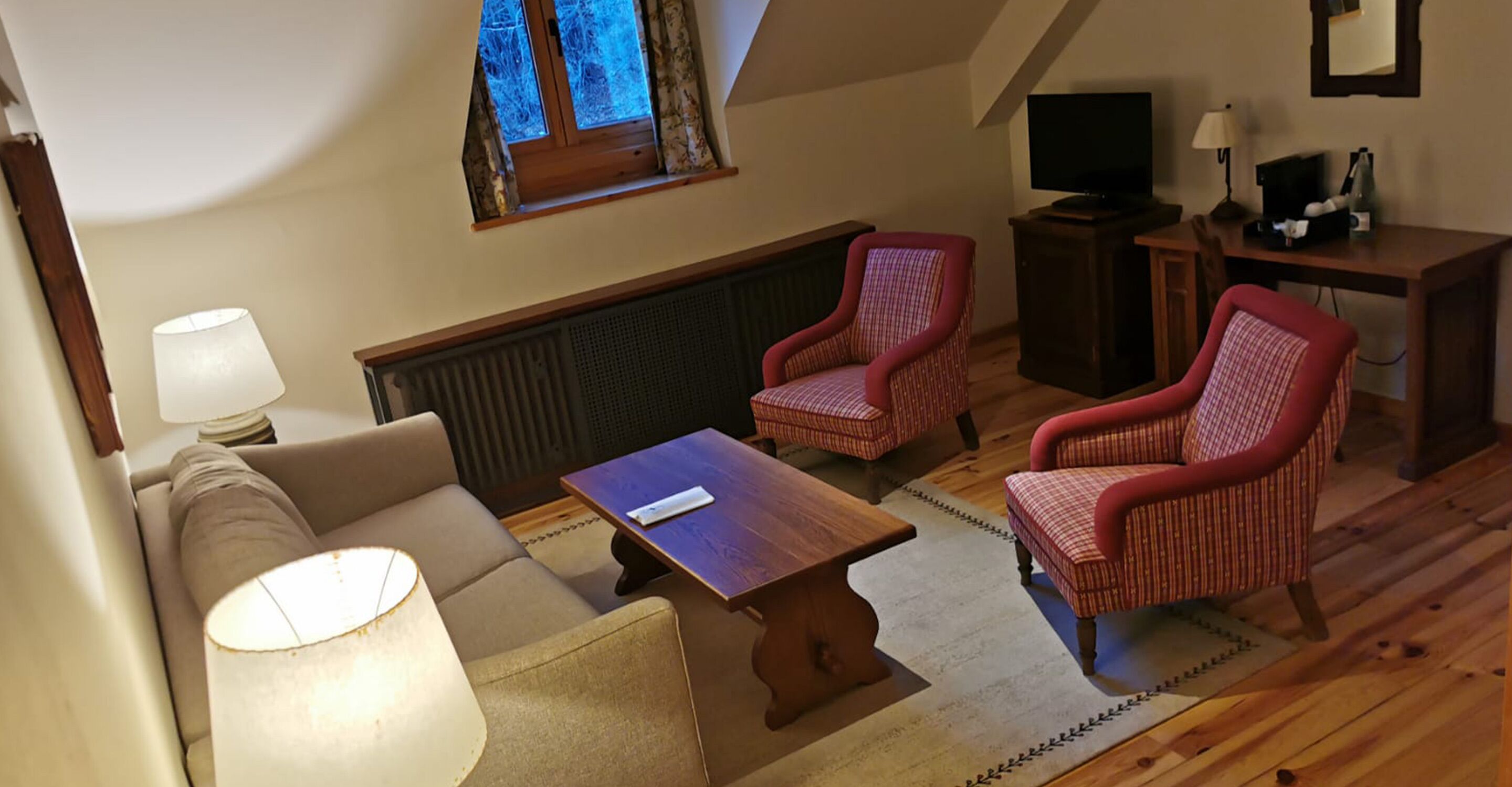 Un salón acogedor con un sofá, dos sillones, una mesa de centro, un televisor y una mesita con una lámpara.